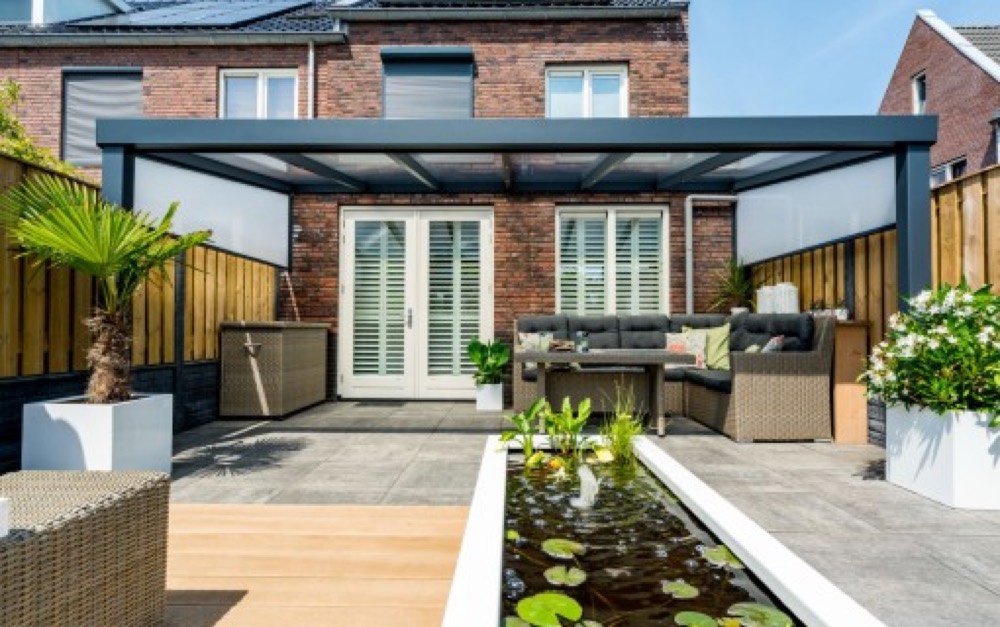 Pergola bioclimatique anthracite adossée à une maison, au-dessus d'une terrasse